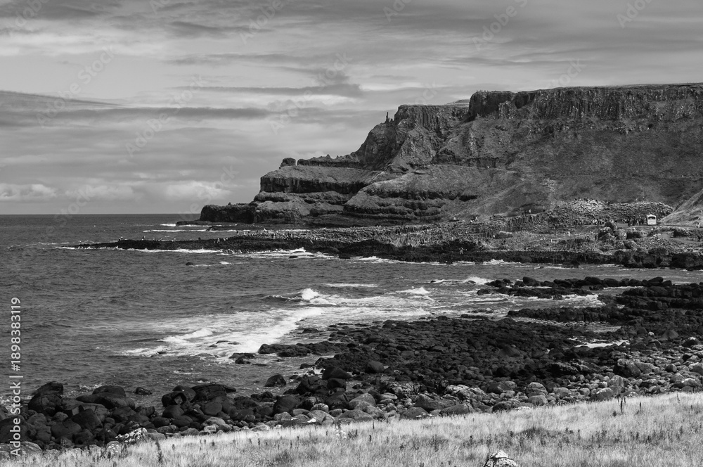 Obraz premium A black and white photo of a rocky shoreline with a calm ocean in the background