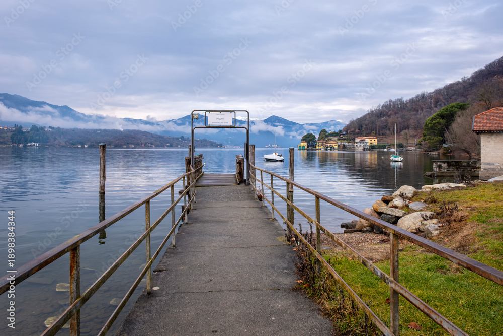 Obraz premium Wooden jetty along the winter water of Orta Lake (piedmont, Northern Italy) with the alps in the background. UNESCO World Heritage Site, its San Giulio island is home to a convent of cloistered nuns.
