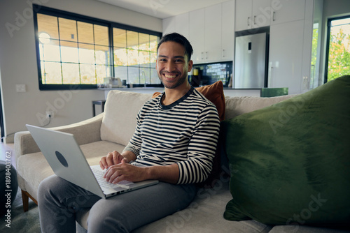 Man comfortably using laptop on couch in house with natural lighting from window