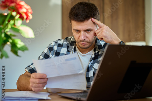 Wallpaper Mural Worried man checking bills and financial papers while sitting at table with laptop. Stressed person planning home budget. Concept of household expenses, budgeting, debt and personal financial stress Torontodigital.ca