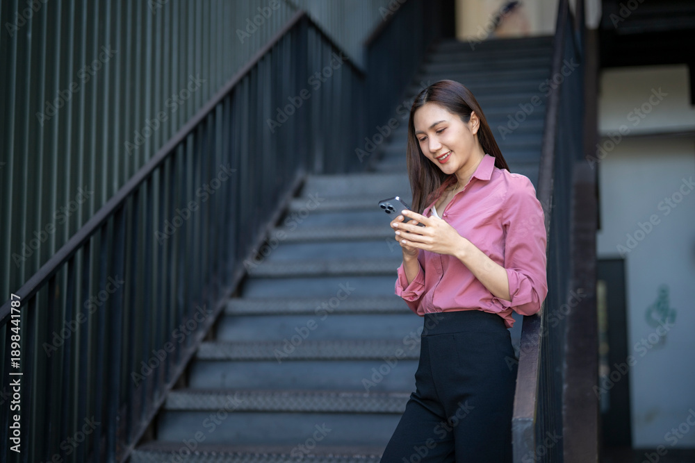 Fototapeta premium Woman smiling using smartphone on urban stairs