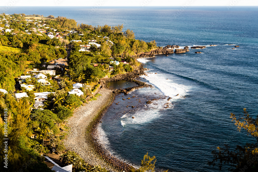 Obraz premium Piscine naturelle sur une plage de galets protégée des vagues devant un village, vue de haut. Manapany les bains, sud île de la Réunion