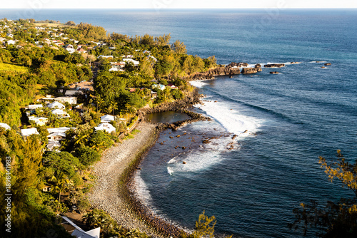 Piscine naturelle sur une plage de galets protégée des vagues devant un village, vue de haut. Manapany les bains, sud île de la Réunion