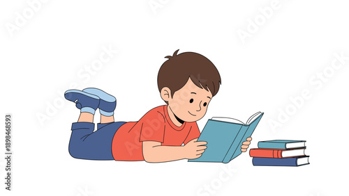 Young boy lying on his stomach on the floor is focused on reading a storybook with a stack of books next to him.