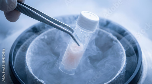 Tweezers lifting a cold vial containing a frozen embryo from cryogenic storage vapor in a sterile laboratory.
