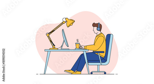 Young man wearing headphones and working intently on his desktop computer at a desk with a lamp and a cup of coffee in his home office.