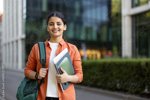 Obraz na płótnie Young indian woman student carrying books smiling on campus