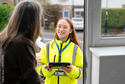 Fotografie Delivery worker greets customer at doorstep with a tablet in hand during a clear