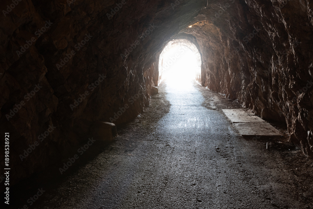Fototapeta premium A dark rock tunnel opens to bright daylight