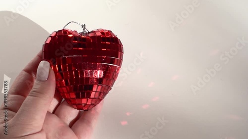 Hand with nude manicure holding glass red  heart on light background, horizontal video