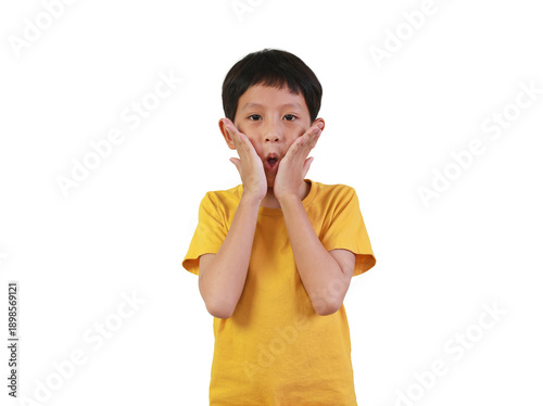 A surprised little Asian boy in yellow t-shirt touching his cheeks with an open mouth and shocked expression, isolated on white background.