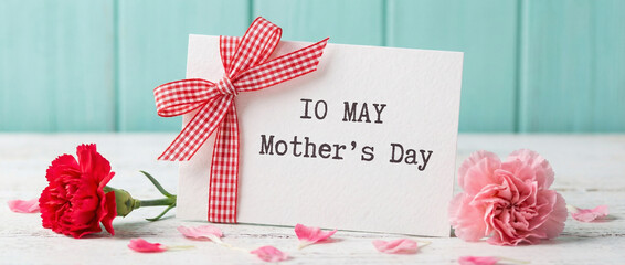 Mothers day greeting card with red and pink carnation flowers on a white wooden table with teal background.