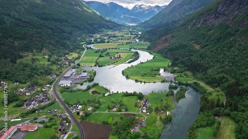 Wide drone panorama of Stryn landscape and river bends. Calm, scenic view of rural Norway with fields, houses, and flowing water framed by steep forested slopes.