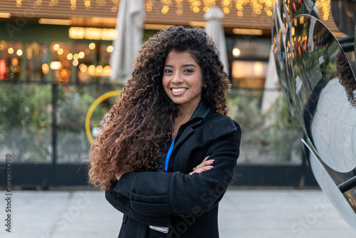 Foto Confident young woman with beautiful curly hair smiling, standing with crossed a