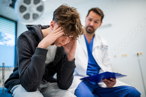 Obraz na płótnie Depressed teenage patient sitting on hospital bed, talking with caring doctor