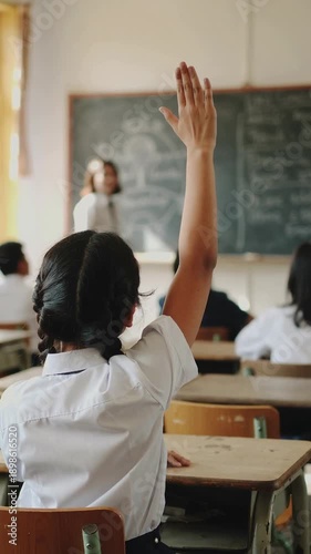 Student girl raising hand in classroom lesson to ask their teacher a question.