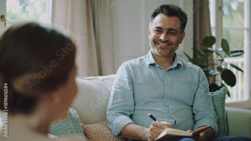 Smiling male therapist taking notes during counseling session from a female patient.