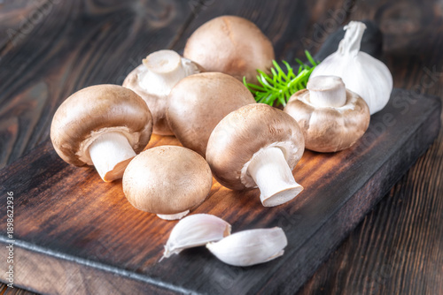 Raw brown champignon mushrooms with garlic and rosemary on rustic wooden board