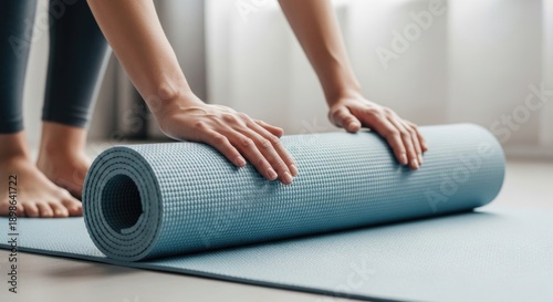 Woman's hands rolling up a blue yoga mat after exercise, close-up view