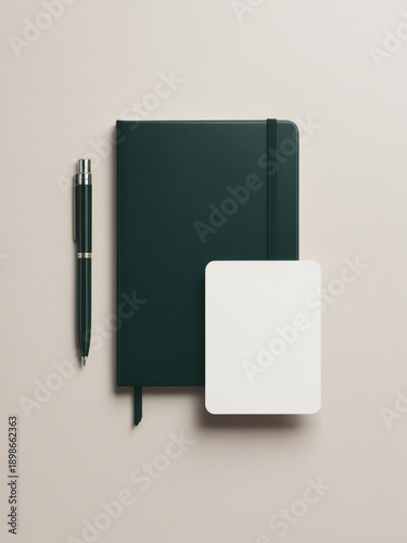 A dark green notebook pen and white notepad on a beige background