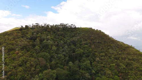 aerial and circular view of a mount at the top advancing with a look at a city in the middle of the Atlantic Forest in Sao Paulo coast in Brazil with mountains at distance