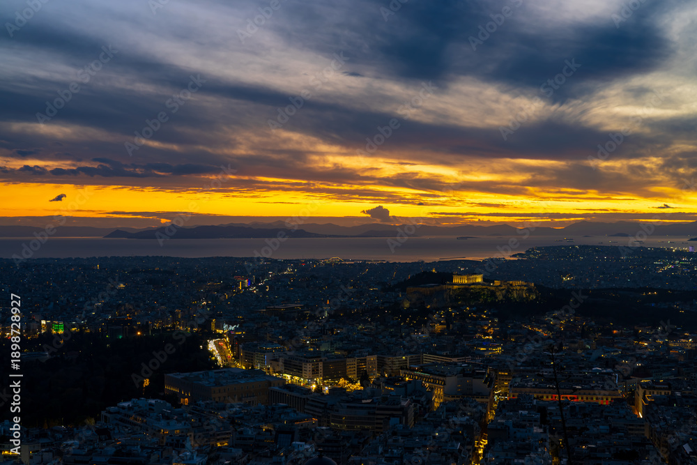 Fototapeta premium Panorama of Athens at sunset with a view of the Acropolis. The city lit up at night against the backdrop of enchanting clouds and a mesmerizing sunset. A peaceful picture of relaxation 