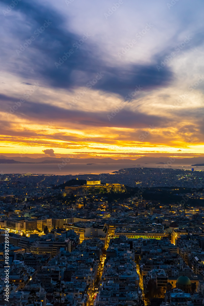 Fototapeta premium Panorama of Athens at sunset with a view of the Acropolis. The city lit up at night against the backdrop of enchanting clouds and a mesmerizing sunset. A peaceful picture of relaxation 