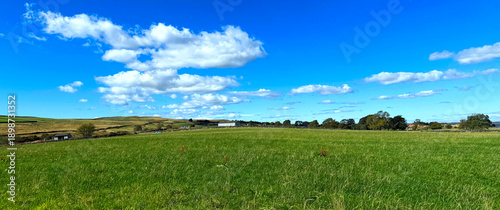 Photography “A green field stretches toward the distant moors, dotted with farm buildings beneath a clear blue sky