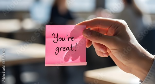 Hand holding pink sticky note with You're great message in office