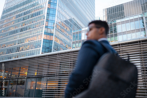 Obraz na plátně A businessman in a suit walks past modern office buildings during early evening