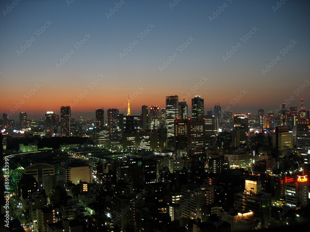 Naklejka premium Tokyo skyline at dusk with illuminated buildings and orange sunset sky