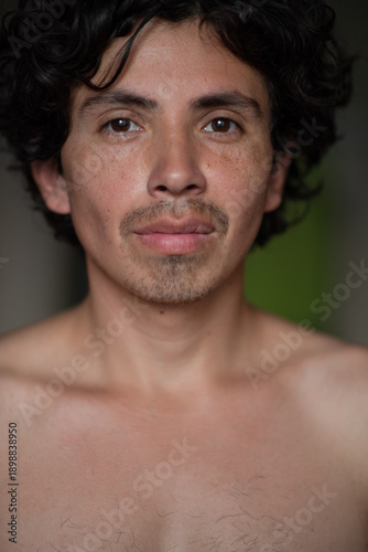 Hispanic male on a dark background. The man smiles and looks at the camera.