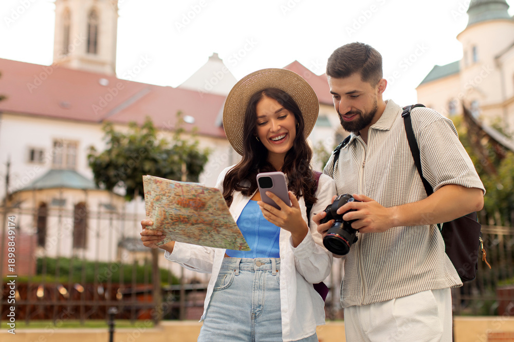 Naklejka premium Couple exploring city, woman holding map and showing cellphone to man, searching route and location while walking together