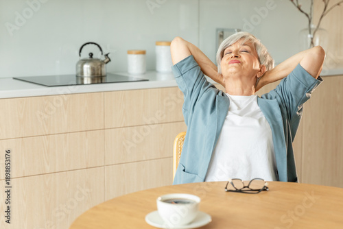 Canvas Print Senior old woman feeling relaxed stretching arms in kitchen at home