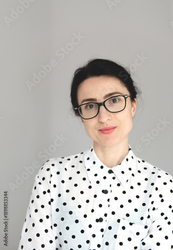 A woman of slim build wearing glasses, smiling and looking at the camera against a neutral background. Portrait of a woman with 