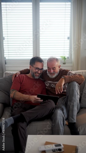 Older father watching sport match on tablet with son.