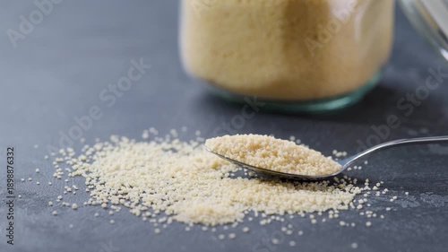 metal spoon with organic couscous on a dark kitchen table. couscous were poured from a glass storage jar into a metal spoon on a dark kitchen table.