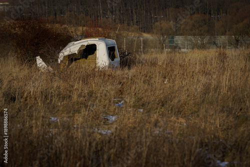 Abandoned white car wreck in tall dry grass field