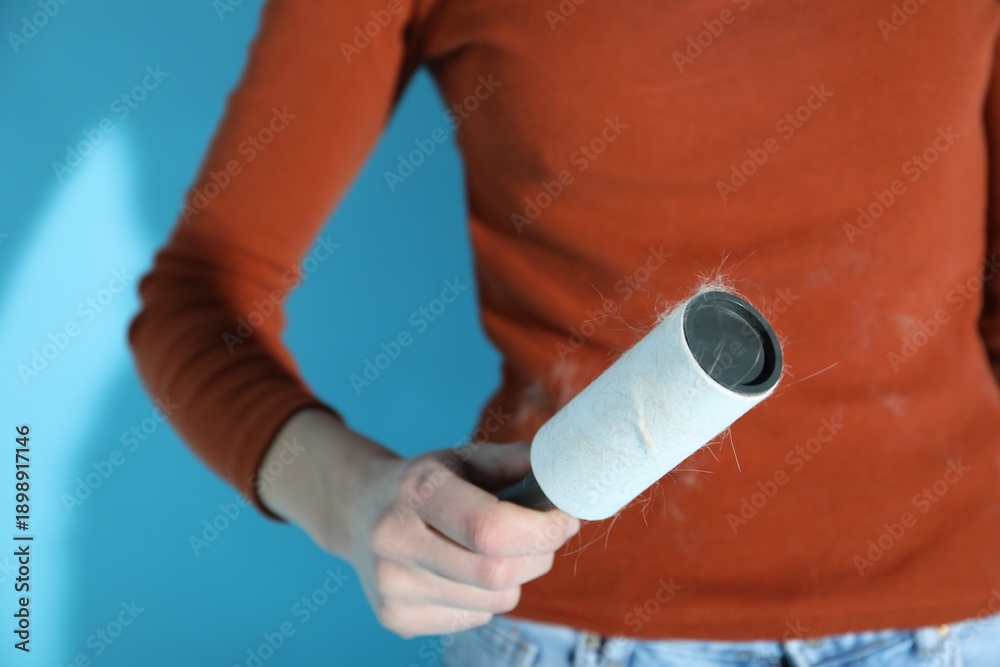 Obraz premium Woman cleaning brown sweater with lint roller on light blue background, closeup