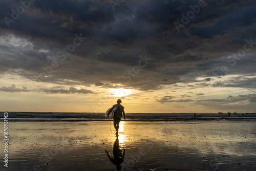 A man carries a surfboard at sunset in Costa Rica.