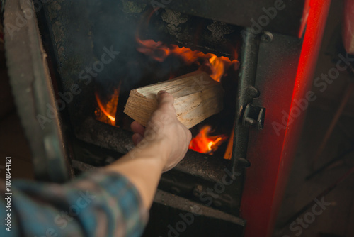 Hand feeding firewood into a burning wood stove