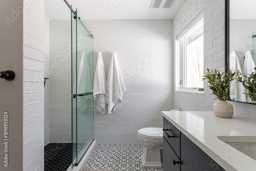 Bright modern bathroom with glass walk-in shower, white subway tile walls, patterned floor and natural light