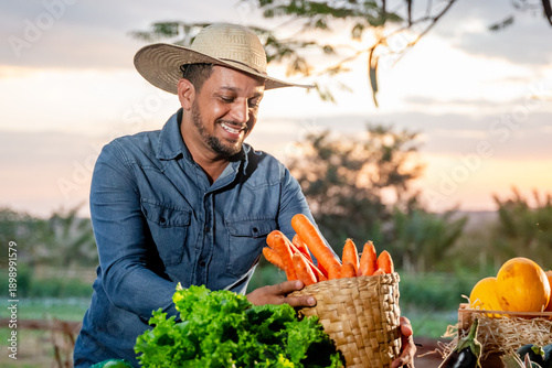 Canvas Print Smiling farmer wearing a straw hat holding a basket of freshly harvested organic