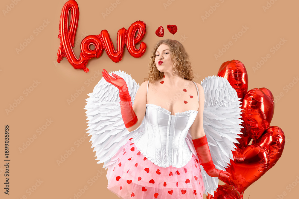 Fototapeta premium Sexy young woman dressed as Cupid with balloons blowing kiss on beige background. Valentine's Day celebration