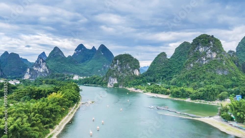 Aerial time-lapse of Li River near Yangshuo Bridge, karst peaks, emerald waters, and bamboo rafts under cloudy sky in Guilin’s iconic landscape.