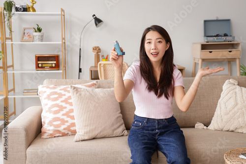 Bild auf Leinwand Happy young Asian woman with inhaler sitting on sofa at home