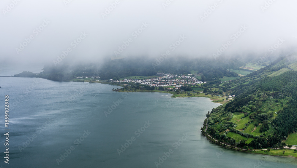 Fototapeta premium Scenic view of Sete Cidades, San Miguel Island, Azores. Twin lakes surrounded by lush greenery and mountains. Misty landscape with a foggy atmosphere.