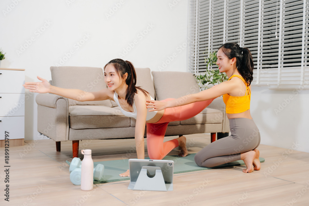 © Nuttapong punna - Two women practicing yoga at home with a personal trainer. Indoor fitness workout, stretching and wellness lifestyle using online guidance