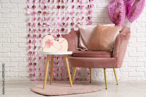 Interior of festive living room with pink armchair, gift boxes, garland and heart-shaped balloons. Valentine's Day celebration