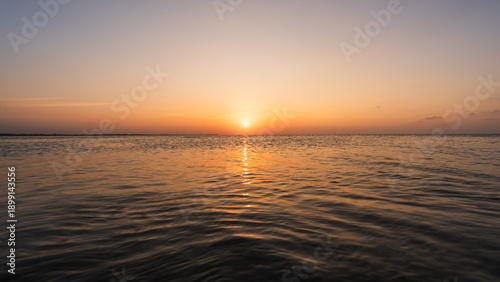 Fotografi Sunset sky clouds over sea water background in evening with orange, blue sun lig